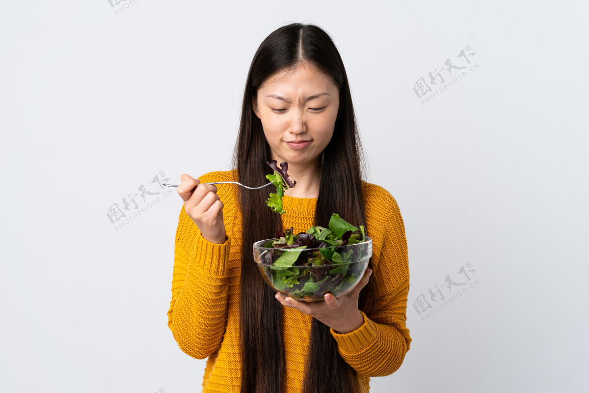 素食孤立的白色背景下 一个年轻的中国女孩拿着一碗沙拉 表情悲伤女士空白美丽