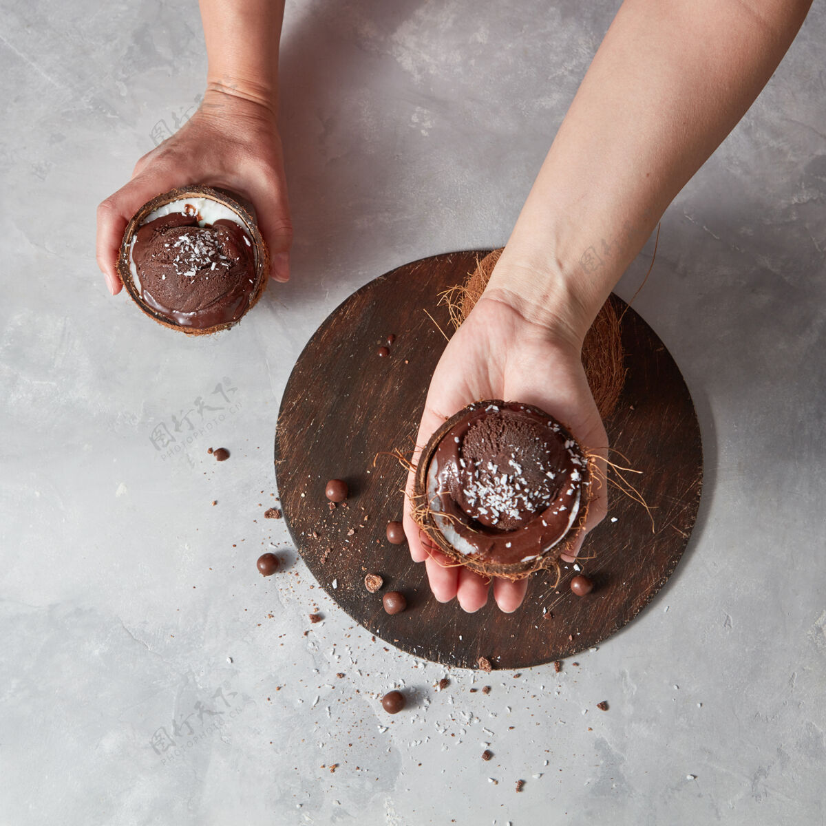新鲜在一张灰色桌子上 一个椰子壳里的自制巧克力甜点 女人的手举在圆板上 桌上放着一个小蛋糕文本.夏季甜点贝壳排毒饮食融化