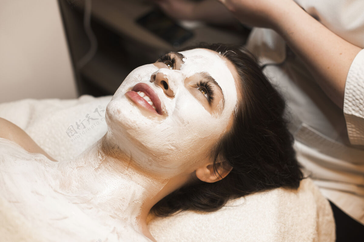化妆品在一个温泉中心 一个美丽的女人靠在一张温泉床上 脸上戴着一个白色的面具特写泥人
