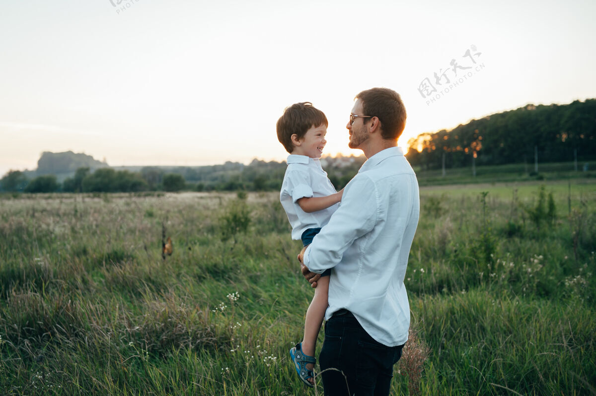 孩子英俊的爸爸带着他可爱的小儿子在绿草如茵的草地上玩耍户外欢呼享受
