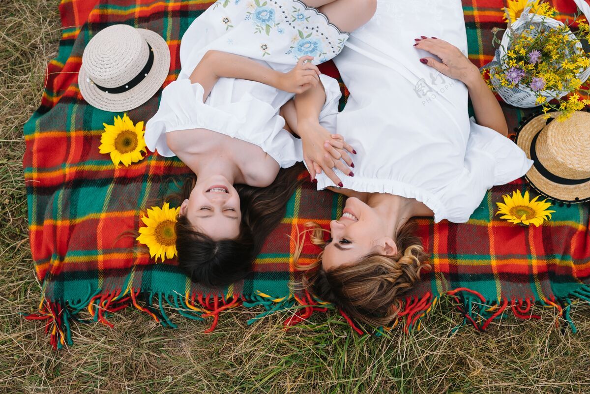 高兴俯视图：快乐的女人微笑着和她可爱的孩子玩耍 躺在户外休闲帽子肩膀