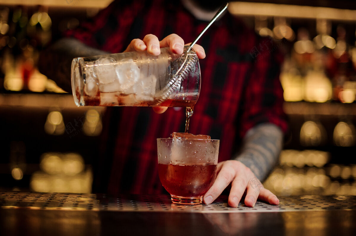 饮料酒保用一个大冰块把新鲜的威士忌鸡尾酒倒进杯子里冷立方体餐厅