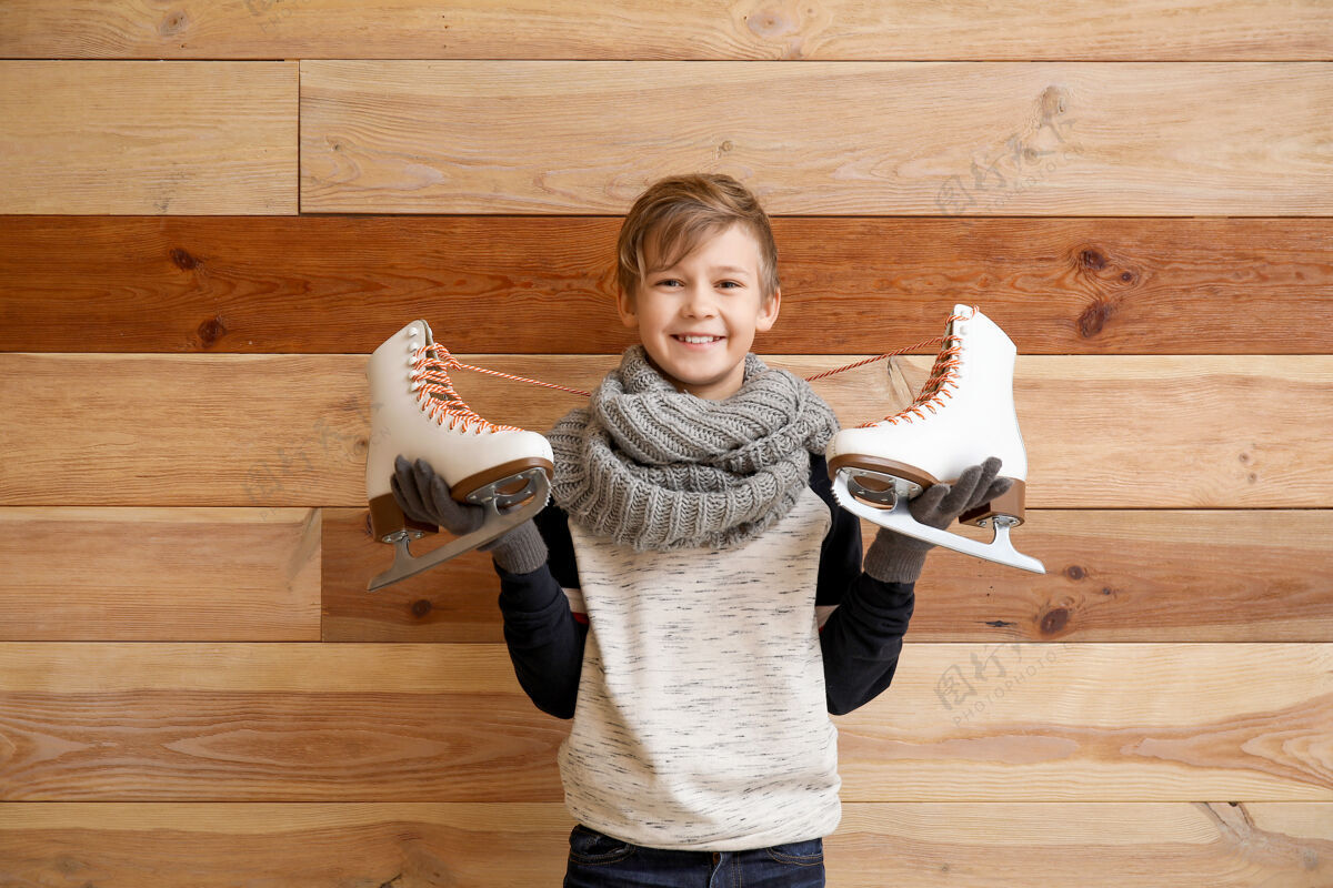 霜冻可爱的小男孩用冰鞋抵着木头运动冰男孩