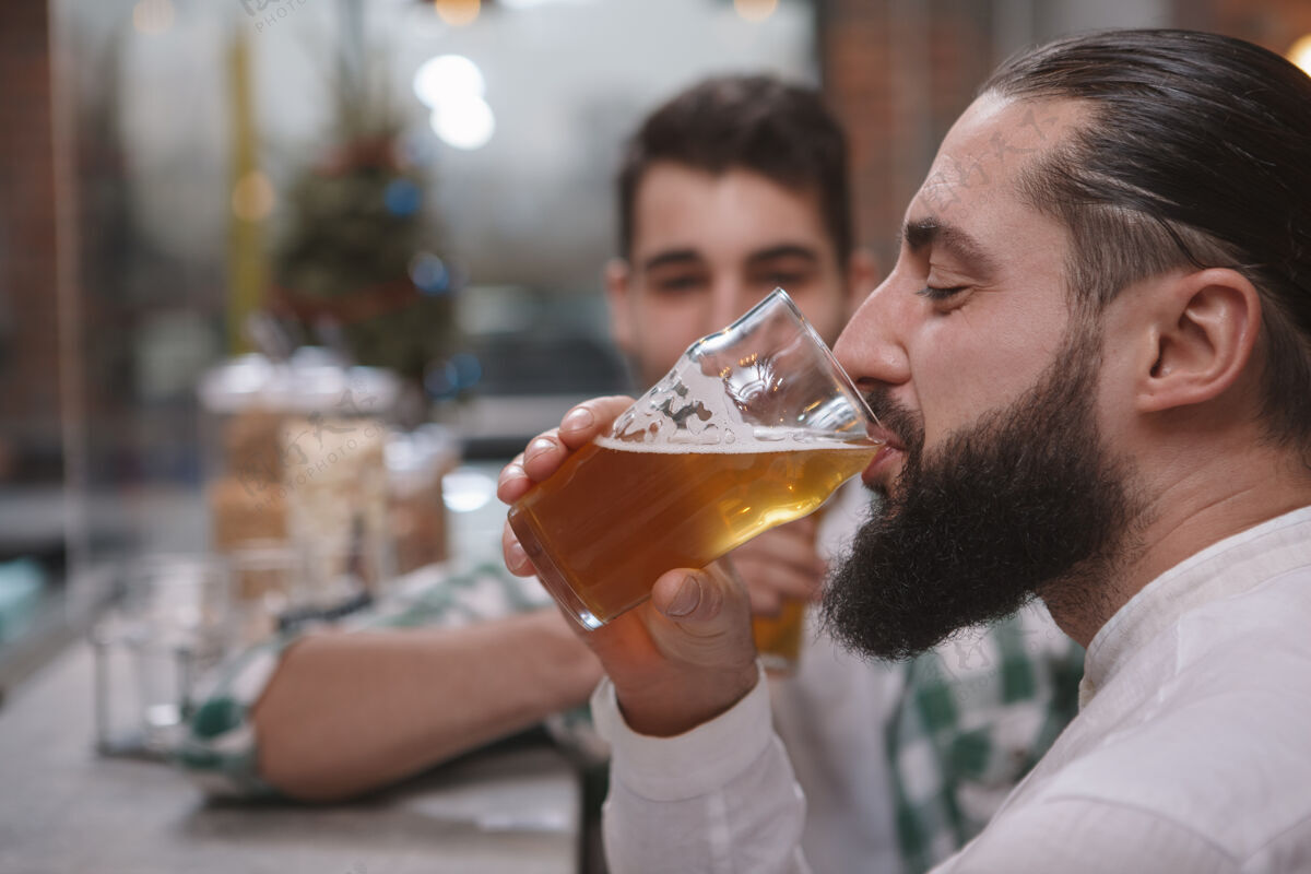 酒吧一个留胡子的男人在酒吧喝淡啤酒的特写镜头朋友饮酒酒吧