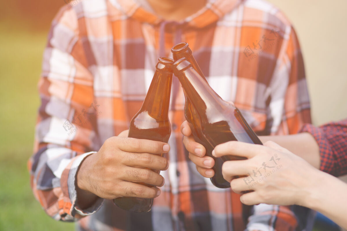 香槟旅行三个年轻的朋友在一起玩 在远足营地放松和喝啤酒干杯瓶节日啤酒饮料