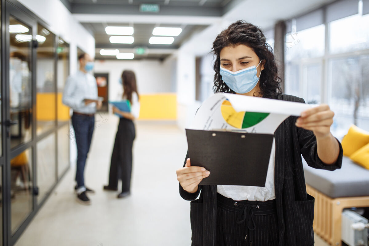 病毒一个年轻的女商人戴着医用口罩 在办公室走廊里查看报纸和商业趋势和前景的画像文件工作场所冠状病毒