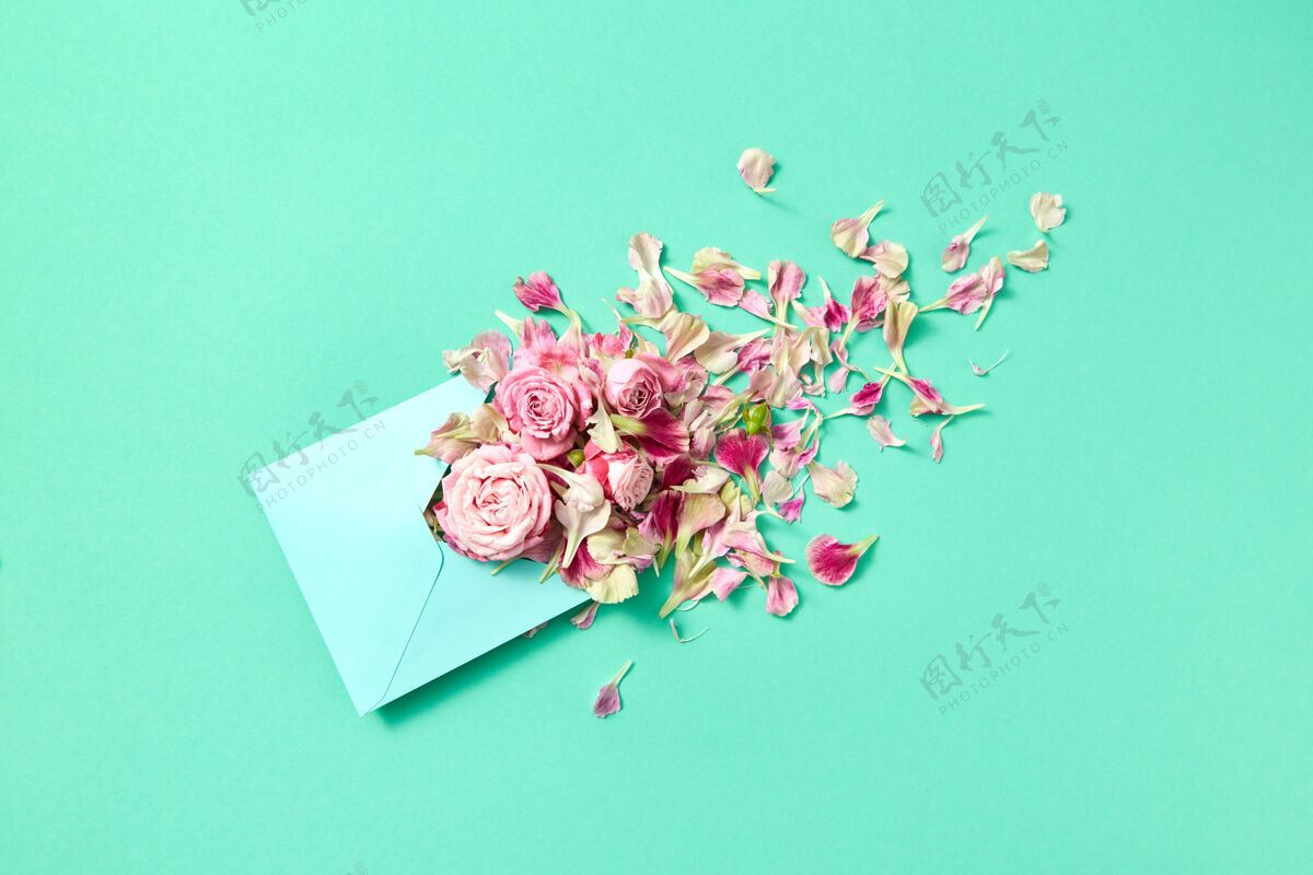 花束带有手工信封的祝贺卡 绿松石色背景上有新鲜的玫瑰和花瓣 复印件空格.top查看粉彩花花朵