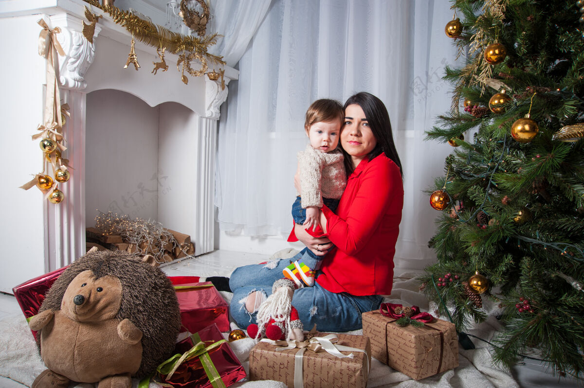孩子妈妈带着她的小儿子在家里靠近圣诞树过圣诞节圣诞树女人年轻