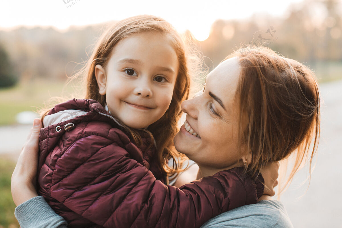 关系美丽的年轻母亲抱着她在公园里微笑的小女孩的特写镜头情绪快乐妈妈