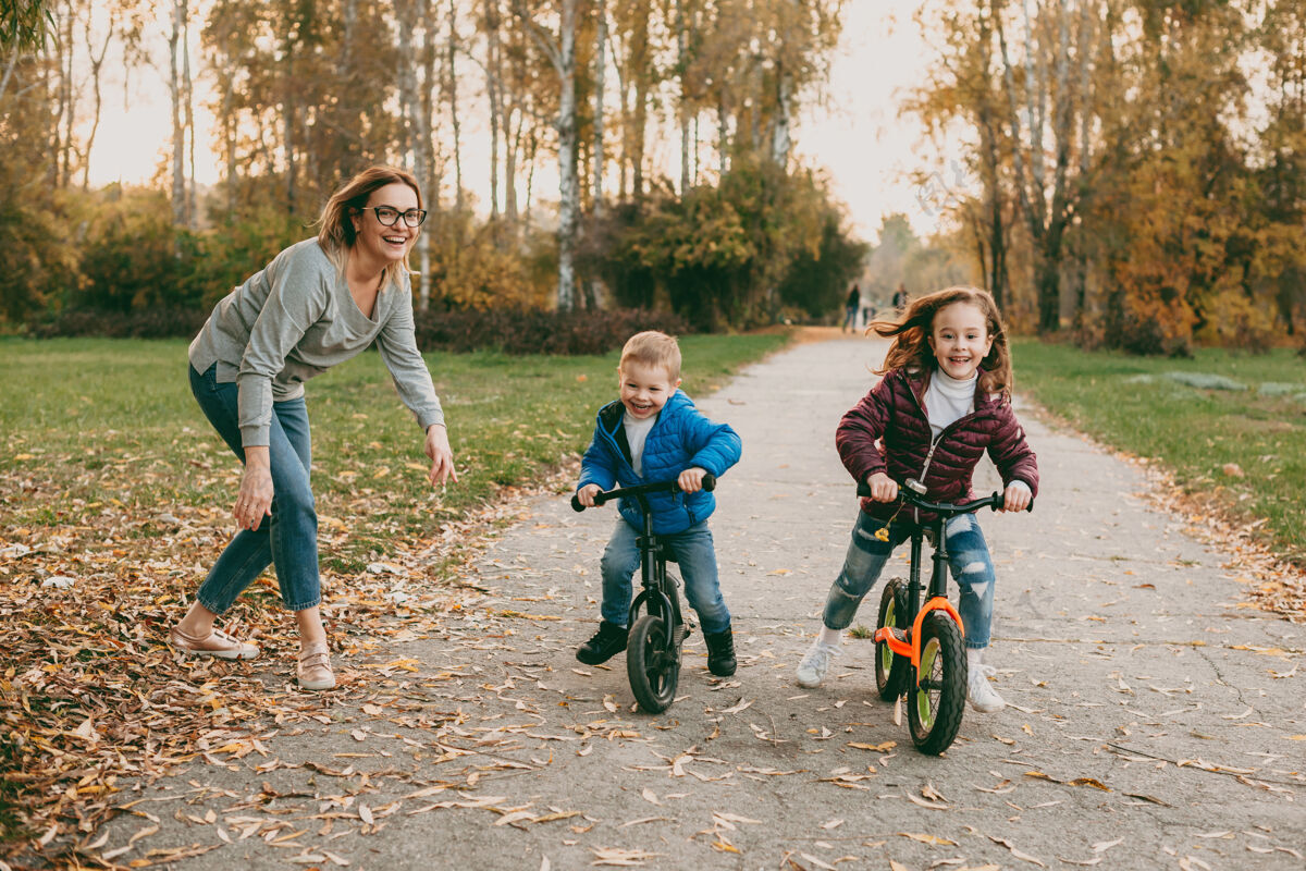 活跃可爱的小弟弟和他的妹妹在公园户外骑自行车比赛 而他们的妈妈正在给他们启动成人父母户外