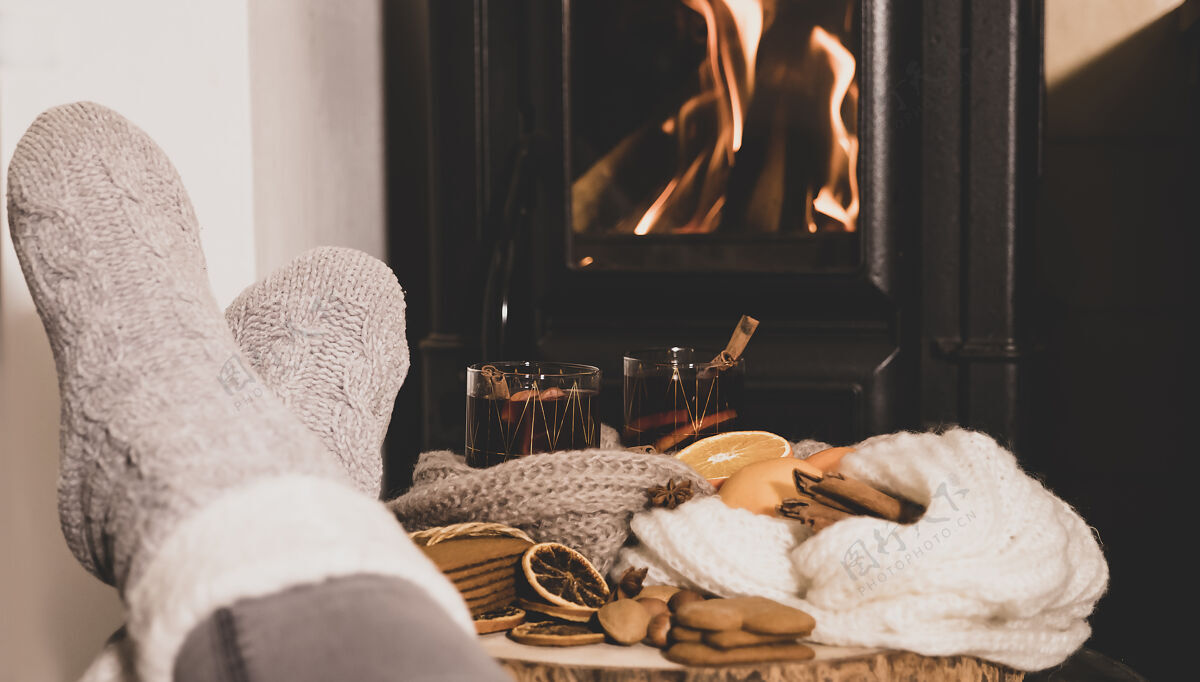 饮料壁炉边放着熟酒 两杯饮料 香料 一条暖和的围巾 脚穿着暖和的袜子 靠近炉子木头室内人