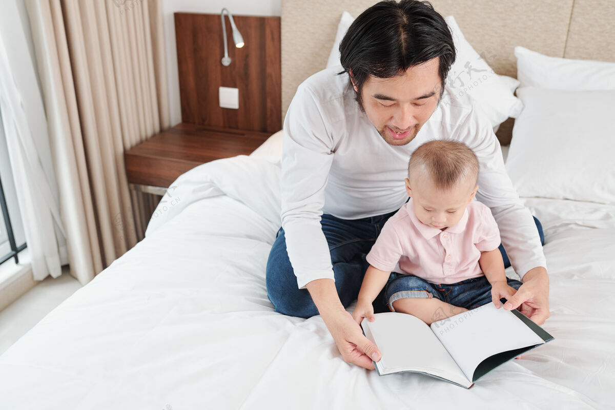 夫妇一个男人和他的小儿子坐在床上 在家里看有趣的书 因为冠状病毒大流行团聚成人书