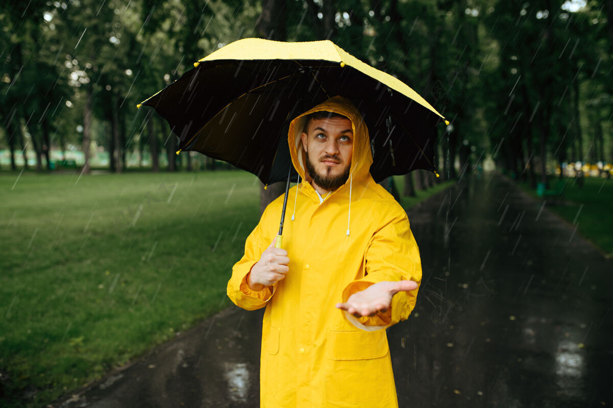 寒冷雨中带伞的人在公园散步白天男性穿着雨衣和胶靴的人 潮湿的天气橡胶雨伞风暴