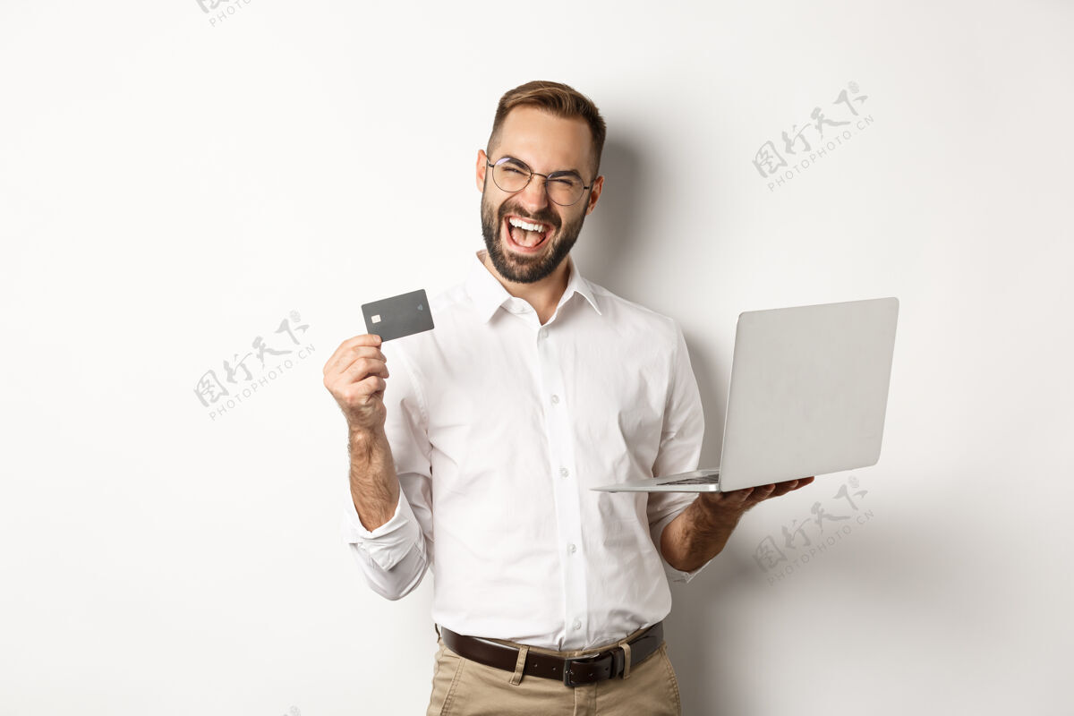 Laptop在线购物帅哥男子出示信用卡 用笔记本电脑在网上订购 站在白色背景上Professional买家房地产经纪人