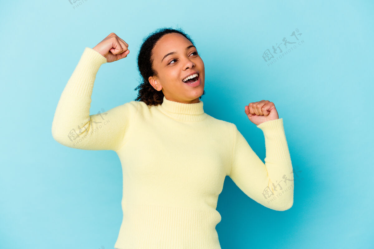兴奋年轻的非裔美国混血女孤立地举起拳头后 一场胜利 赢家的概念蓝色拳头卷发