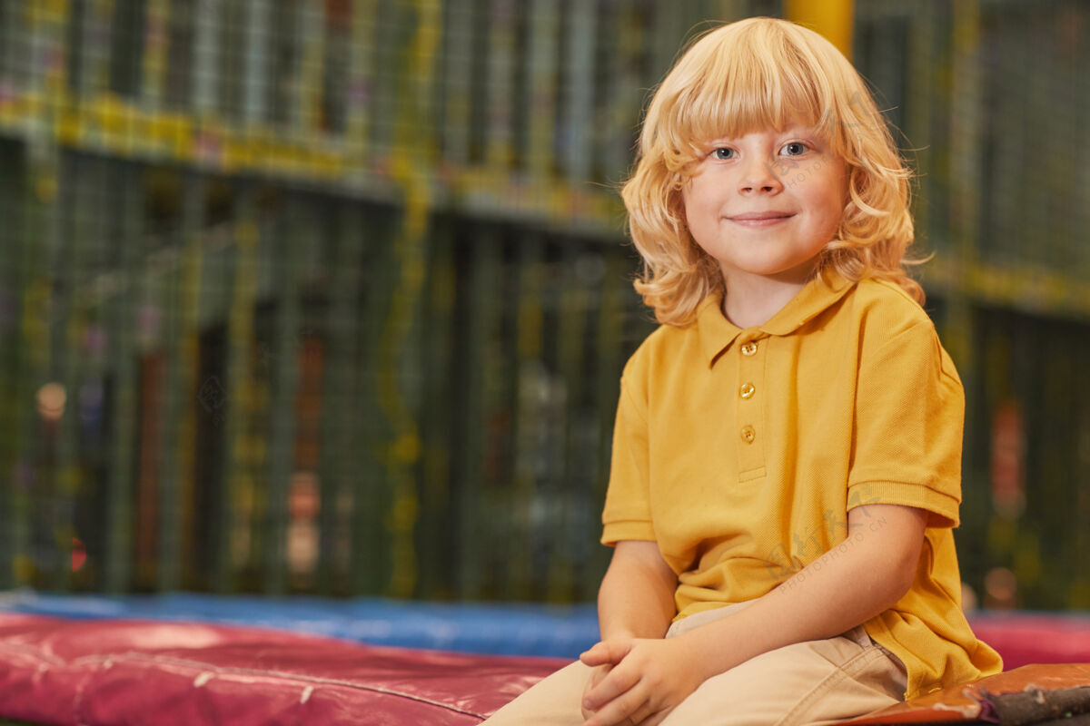 幼儿公园里坐在蹦床上金发小男孩的画像特写快乐肖像