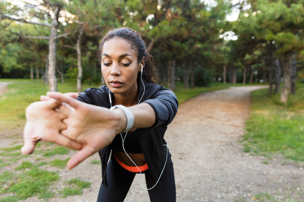 公园20多岁的女运动员穿着黑色运动服 在绿色公园里锻炼身体听力非洲黑发