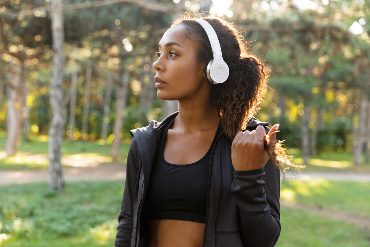女性一位20多岁的女运动员穿着黑色运动服 戴着耳机 穿过绿色公园训练女性女性
