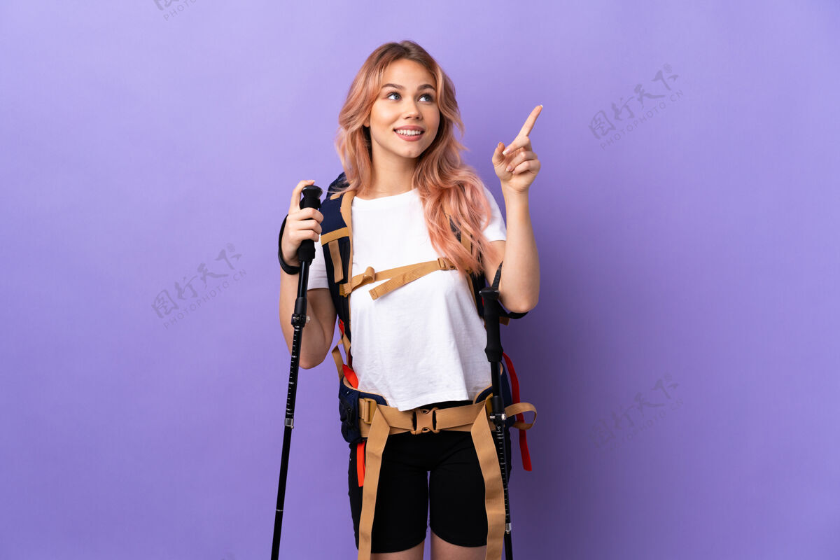 运动女孩背着背包和登山竿在孤立的紫色食指上指指点点是个好主意小径徒步旅行想法