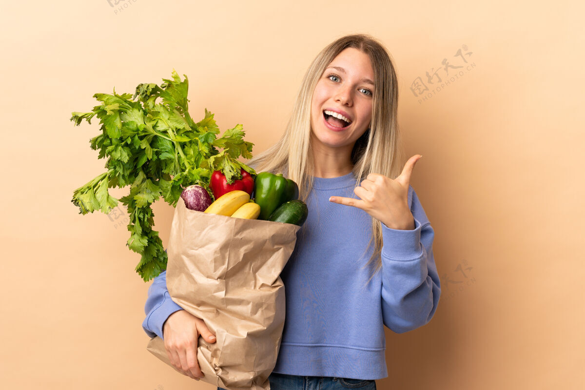 购买年轻的金发女郎拿着装满蔬菜的袋子隔着隔离墙打电话电话购买交谈