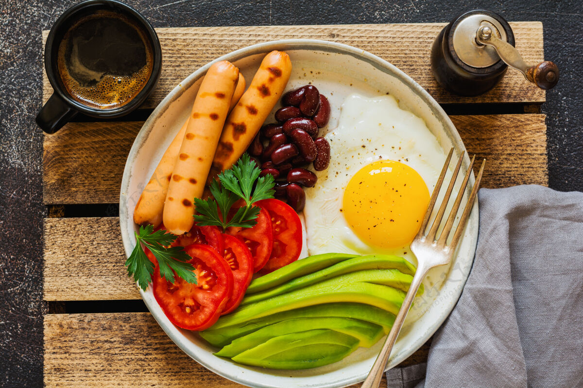 欧芹传统的英式早餐 油炸鸡蛋 鳄梨 烤香肠 豆子和西红柿放在深色的混凝土表面肉吐司叉子