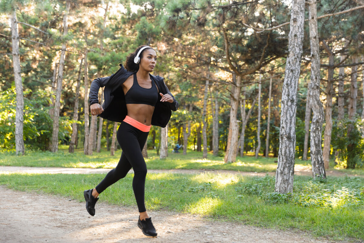 年轻一个20多岁的美国女人穿着黑色运动服 戴着耳机 在绿色公园里跑步早晨非洲运动员