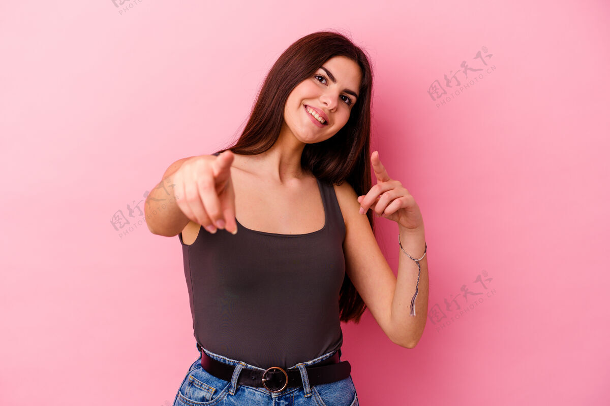 前面年轻的白人妇女孤立在粉红色背景中 微笑着指着前面年轻点选择
