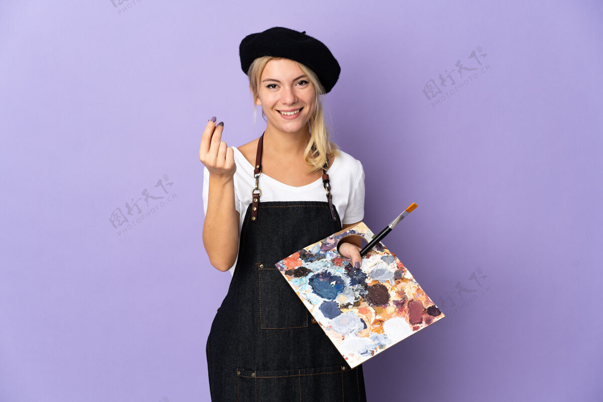 女性年轻的艺术家俄罗斯女子拿着一个调色板孤立在紫色背景上赚钱的手势创意画笔俄罗斯