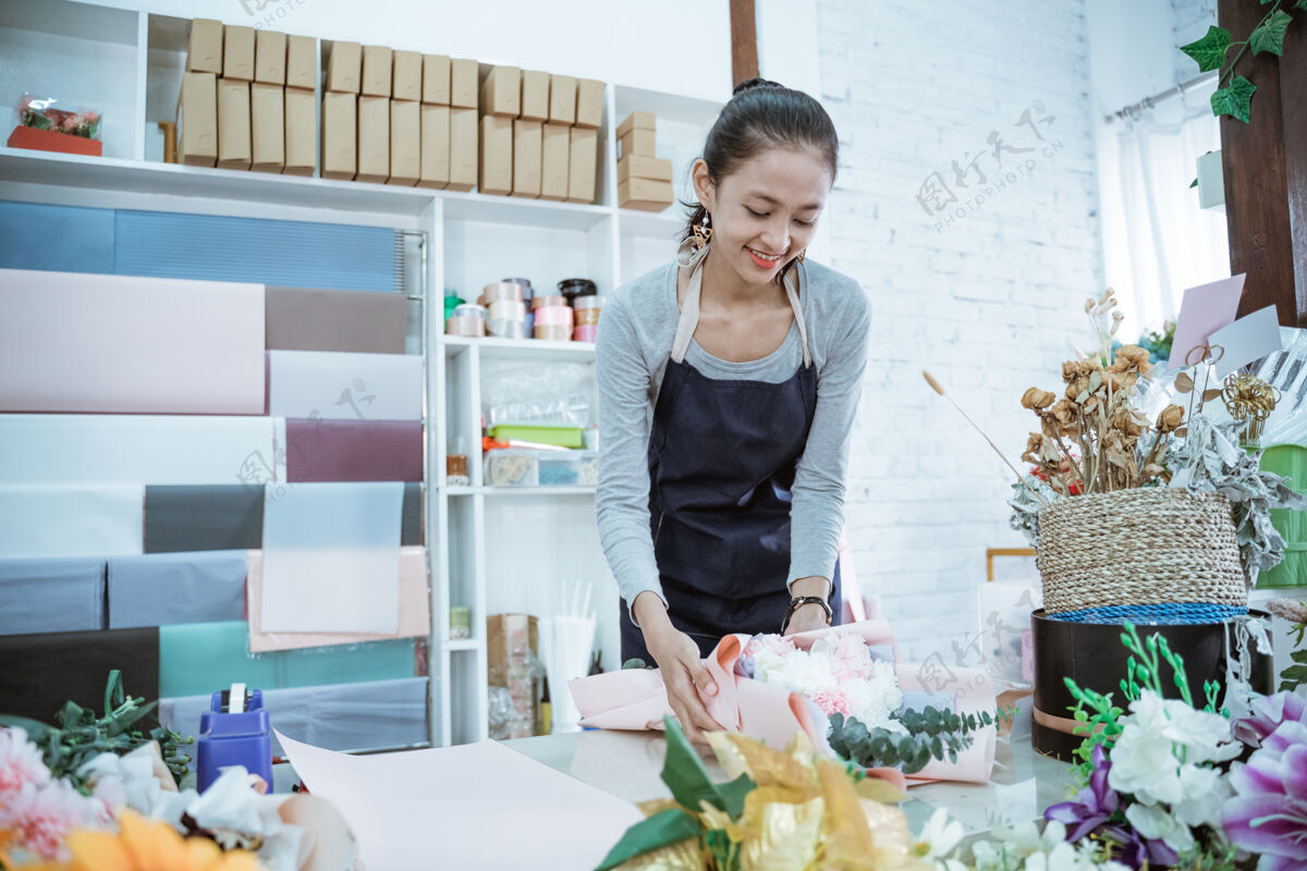 女人在花店工作的年轻女花匠在桌子工作区定做法兰绒花商业开花女性