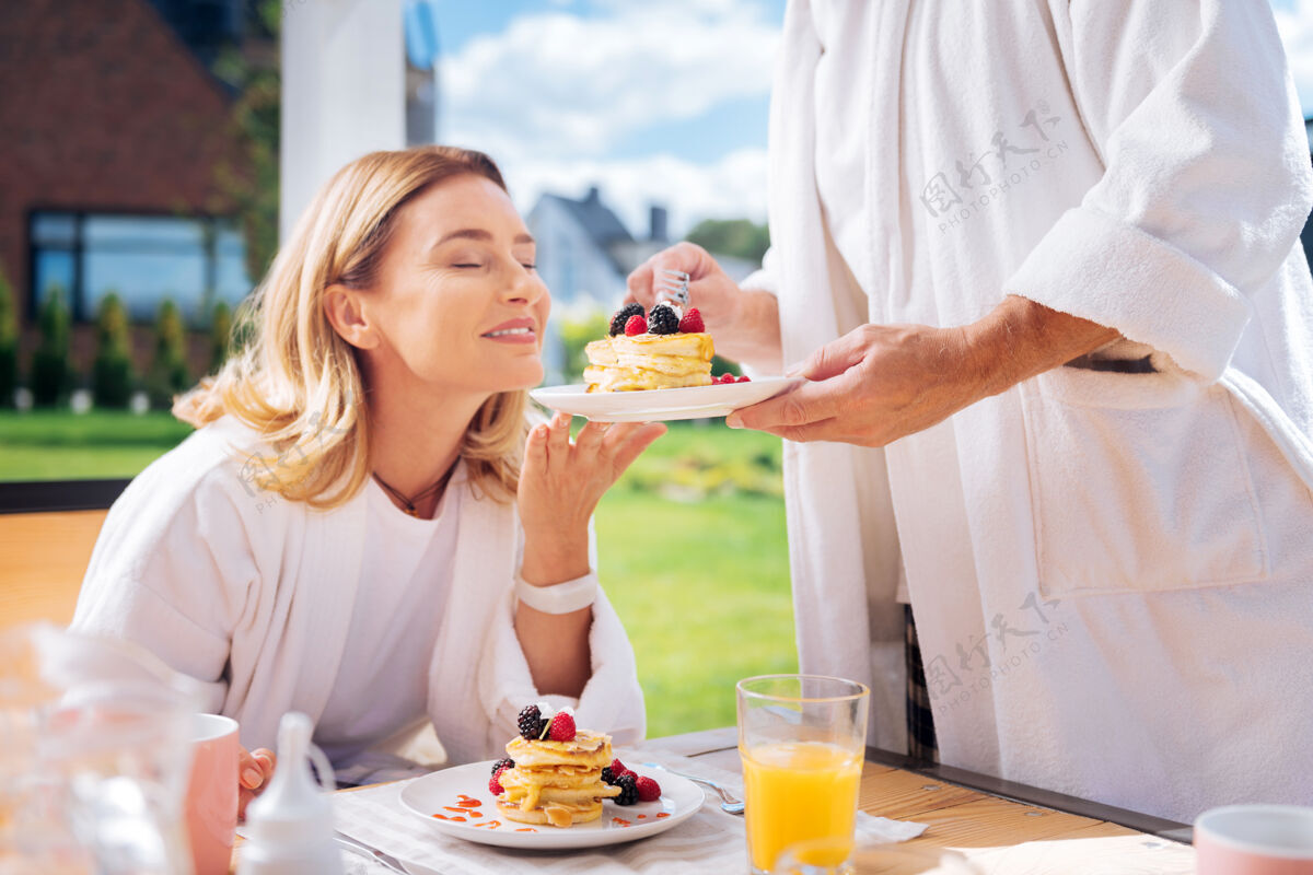 运动热煎饼金发女人和丈夫一起吃早餐时 闻着上面有水果的热煎饼爱情氛围天气