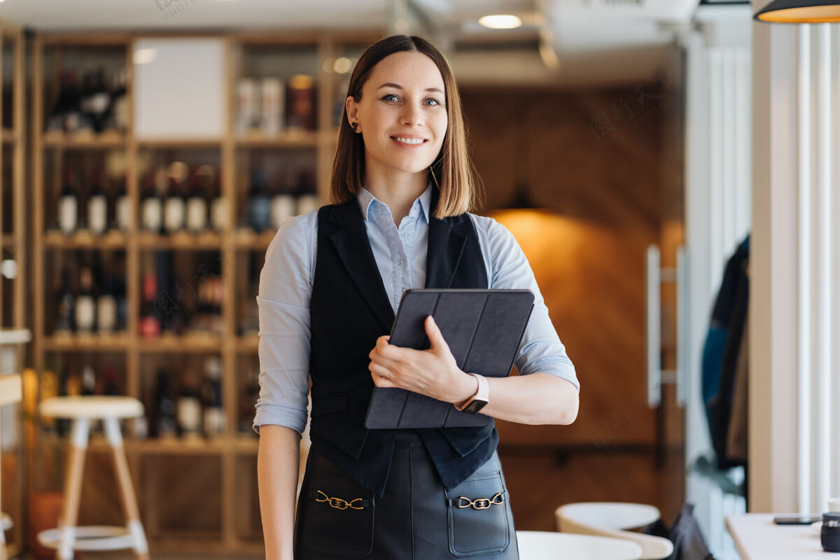 年轻一位年轻漂亮的女士站着 手里拿着一个数字平板电脑hands.business老板 餐厅 餐厅人公司员工