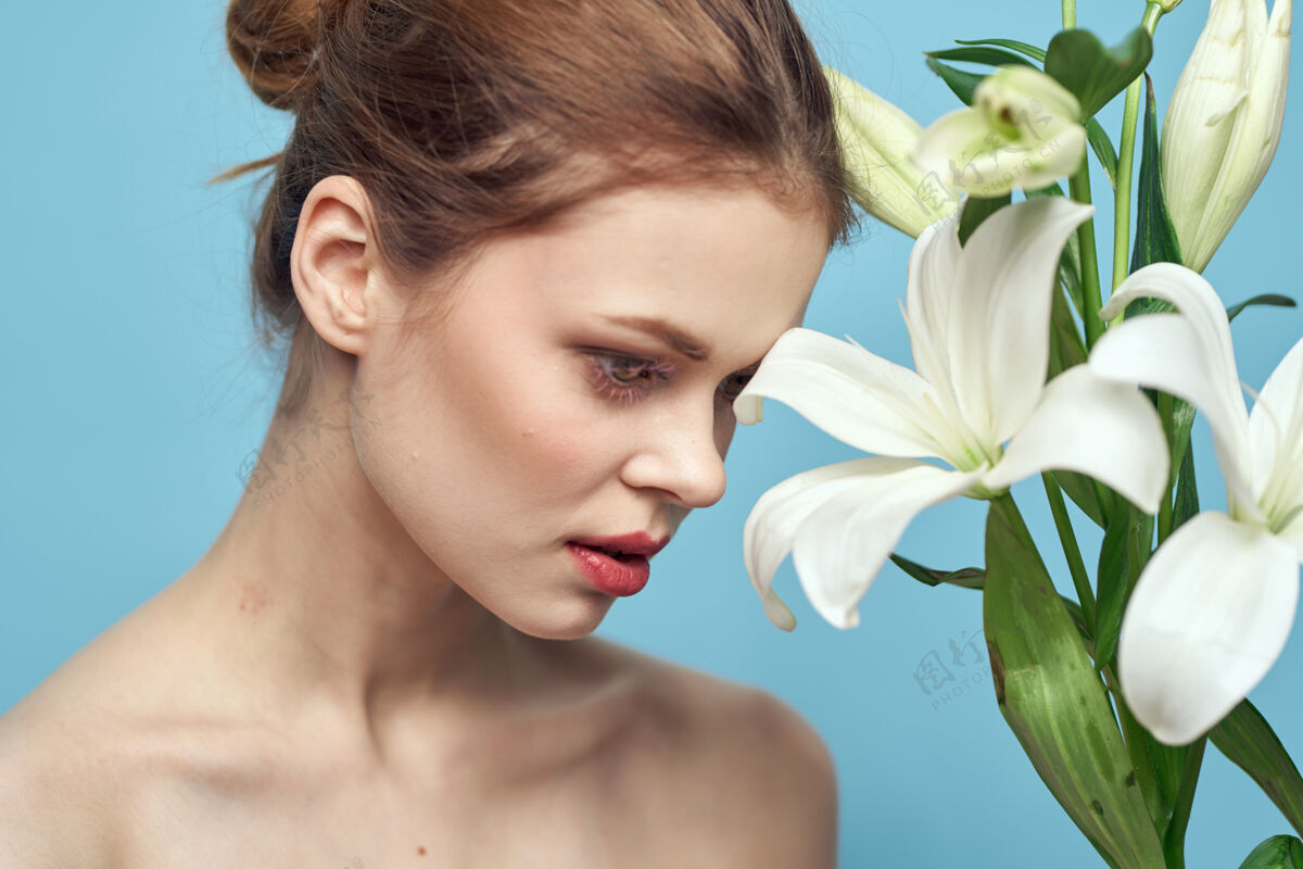 化妆蓝色墙上开着白花的女人剪下的风景百合肖像人