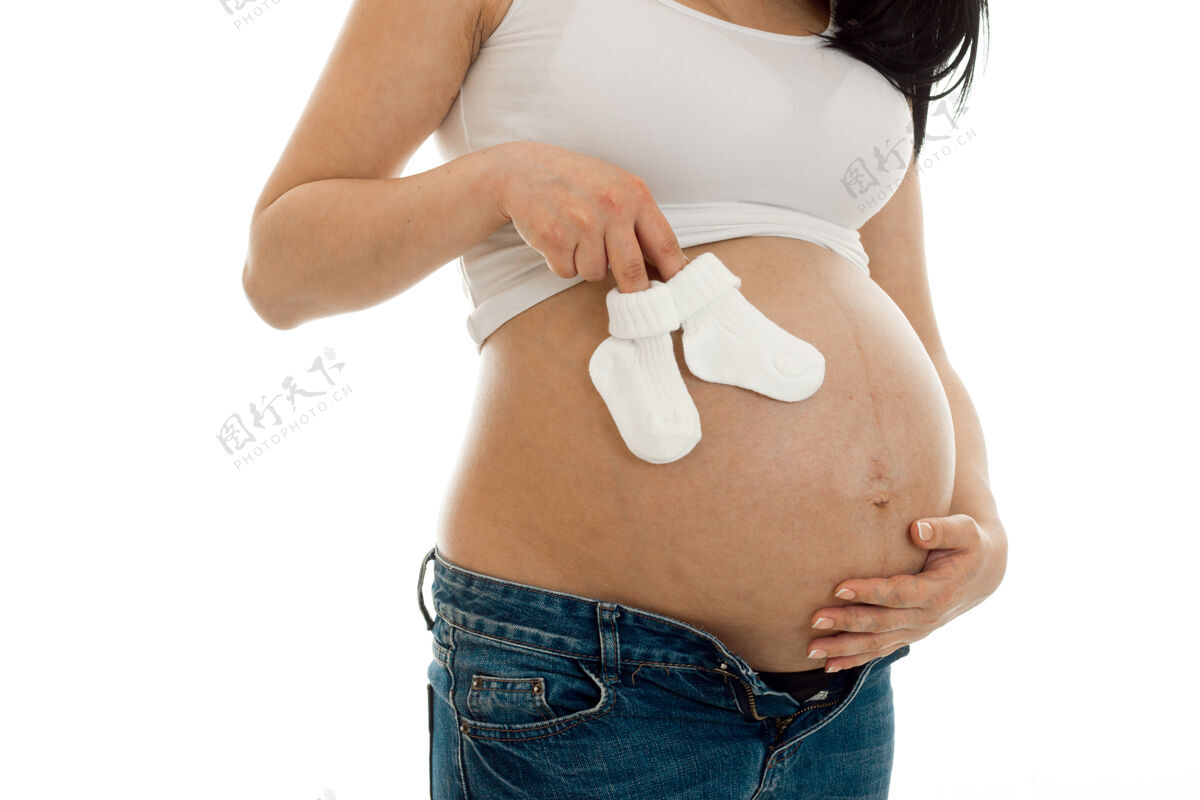 快乐一个年轻的孕妇穿着白衬衫 手里拿着小袜子 孤零零地站在墙上皮肤为人父母孩子