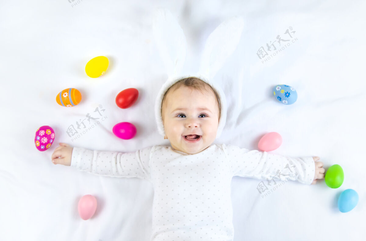 肖像宝宝穿得像兔子 在白色的表面上放复活节彩蛋毯子人有趣
