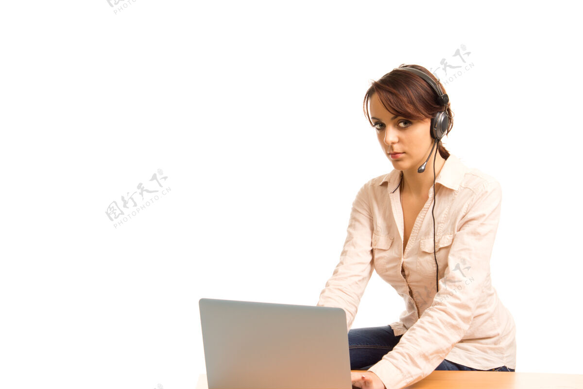 工人年轻迷人的私人助理或接待员 戴着耳机 坐在桌旁的笔记本电脑旁工作女士笔记本电脑服务