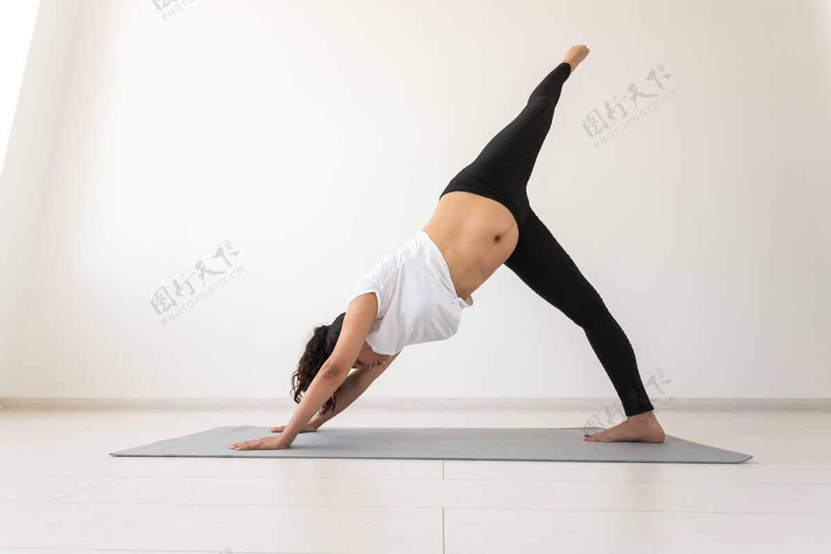 快乐年轻灵活的孕妇在地毯上做体操 在白墙上的地板上的概念中年责任女人