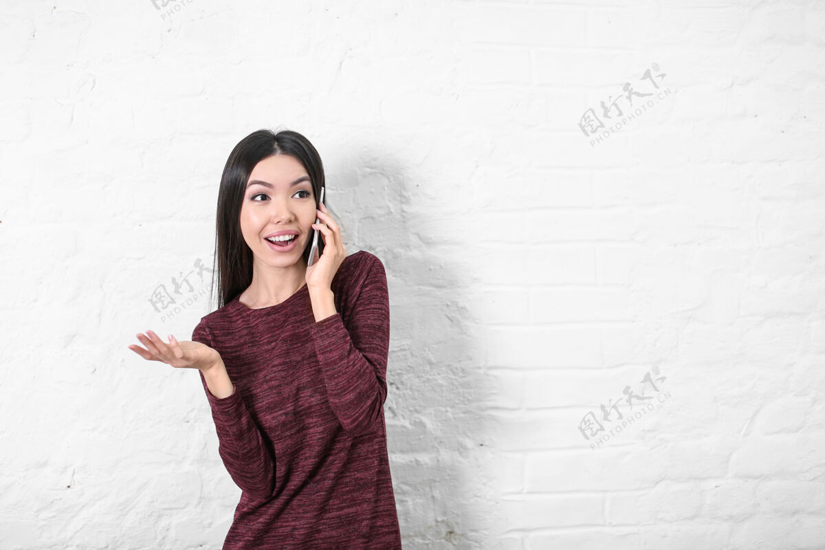 女人快乐的年轻女子在白墙附近用手机交谈手机休闲成人