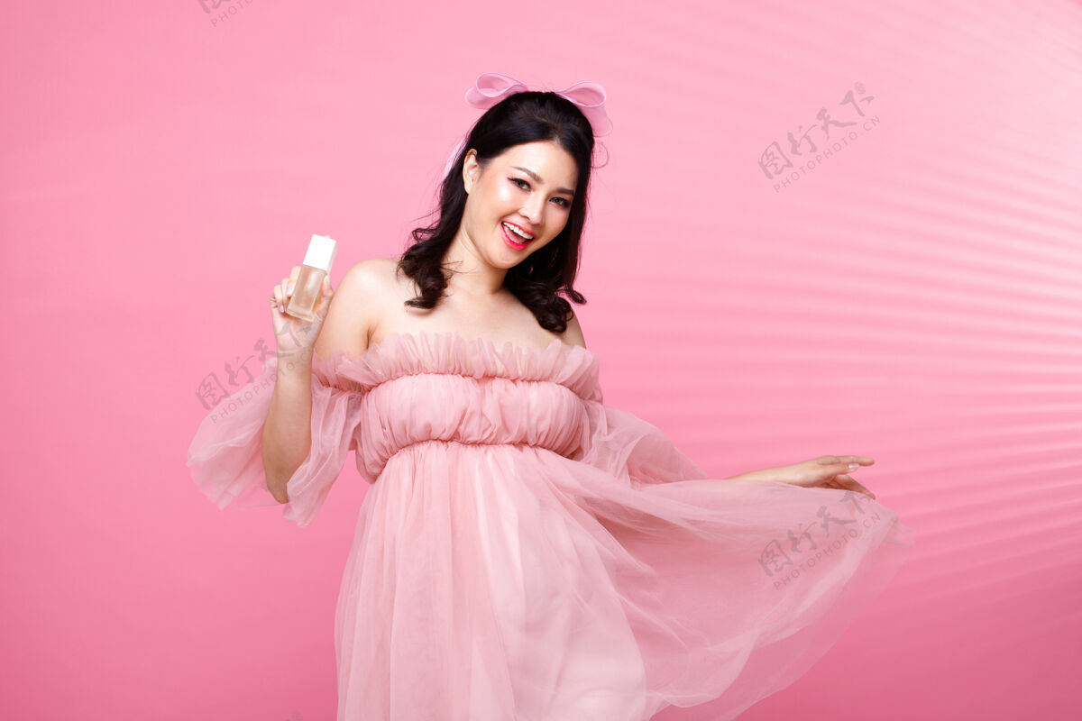 感情时尚美女有黑发表示心情愉快爱亚洲人女孩穿粉色连衣裙在粉色调的墙上捧着美容护肤液 敷在脸上 手抄空间肖像脸半身