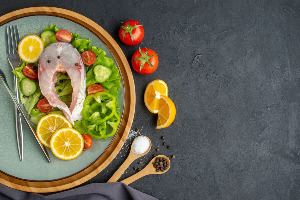 壁板上图：生鱼片和新鲜蔬菜柠檬片和餐具放在灰色盘子上香料深色毛巾放在黑色表面左侧晚餐生鱼食物