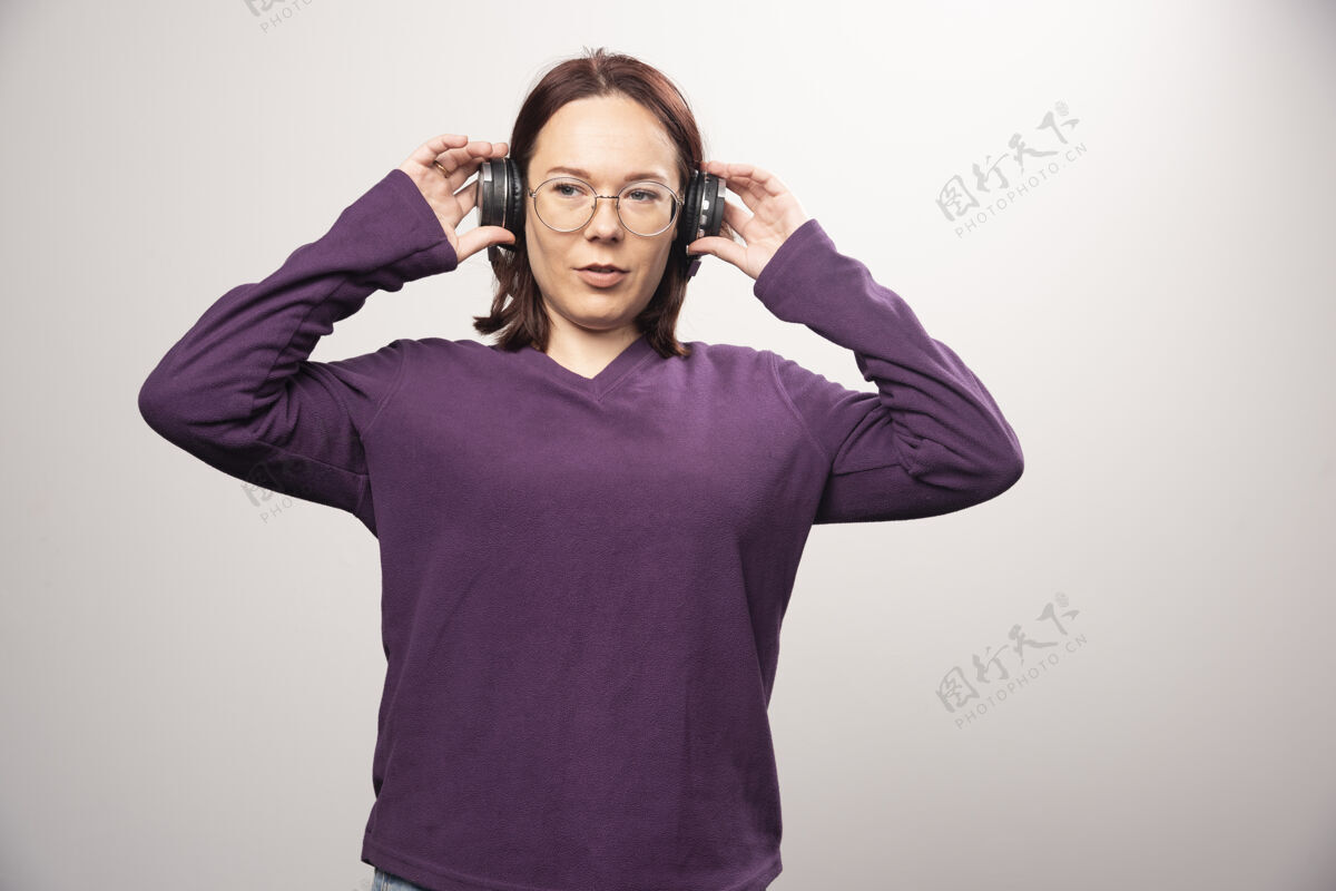 站立戴着眼镜的年轻女子戴着耳机在听音乐 这是一张高质量的白色照片时尚女人肖像