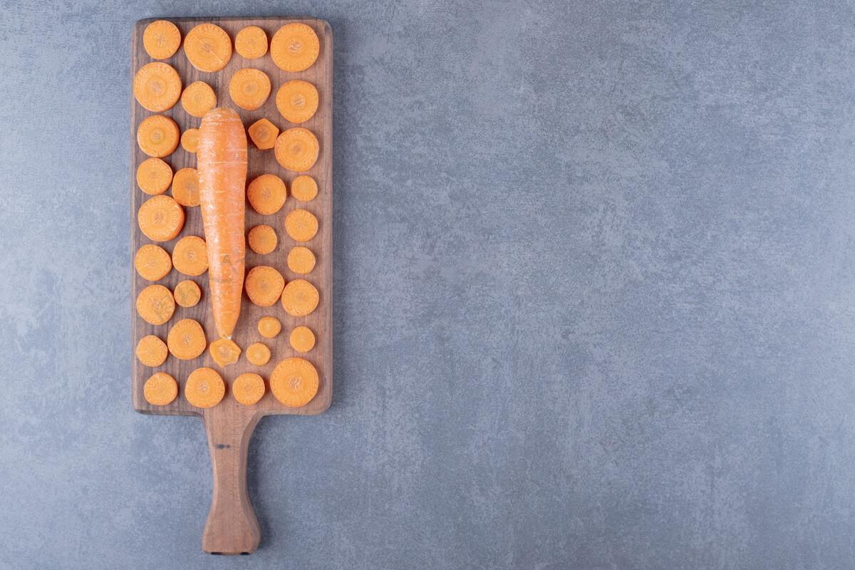 营养在大理石的背景上 放着一块切成薄片的整根胡萝卜的木板美味托盘块
