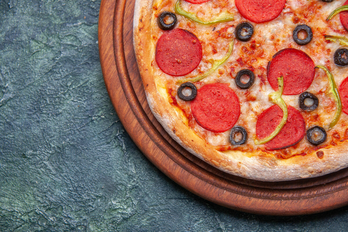 晚餐在深蓝色表面左侧的木制砧板上近距离观看美味的比萨饼 并提供免费空间左胡椒上