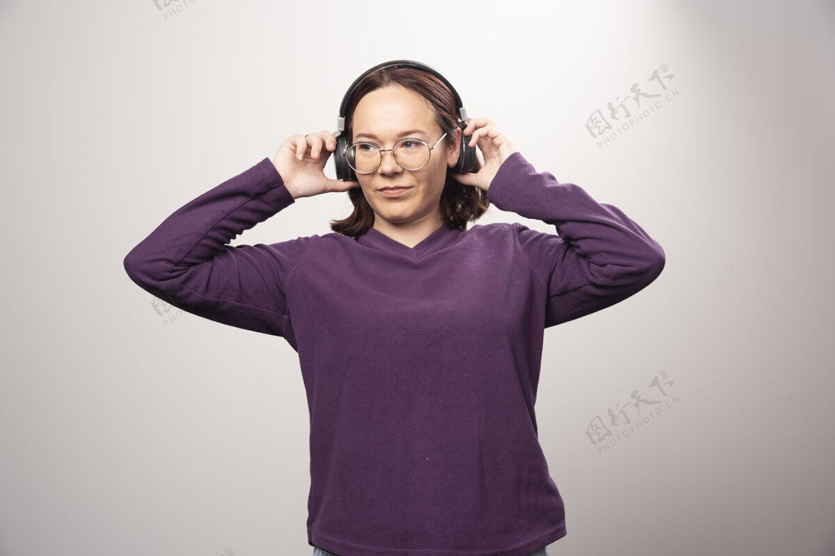 青春戴着眼镜的年轻女子戴着耳机在听音乐 这是一张高质量的白色照片姿势时尚女士