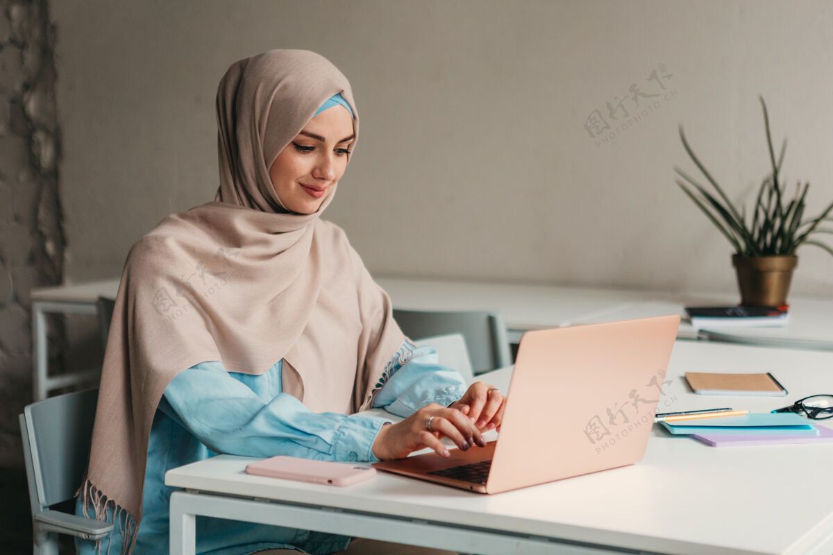 阿拉伯语年轻漂亮的现代穆斯林妇女戴着头巾在办公室的笔记本电脑上工作 教育在线办公桌互联网围巾