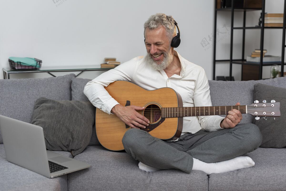 成熟老人在家的沙发上用笔记本电脑学习吉他课成人沙发室内