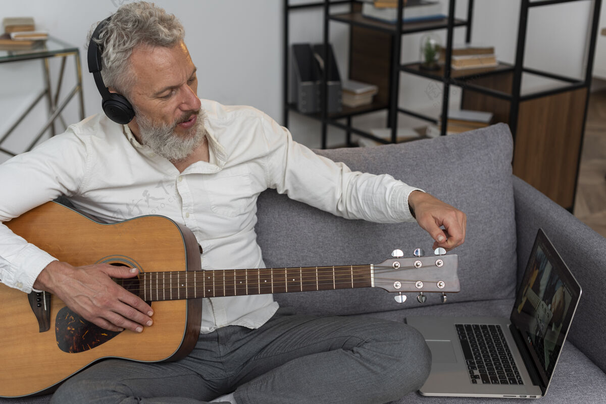 老年人老人在家的沙发上用笔记本电脑学习吉他课原声吉他灰色头发老年人