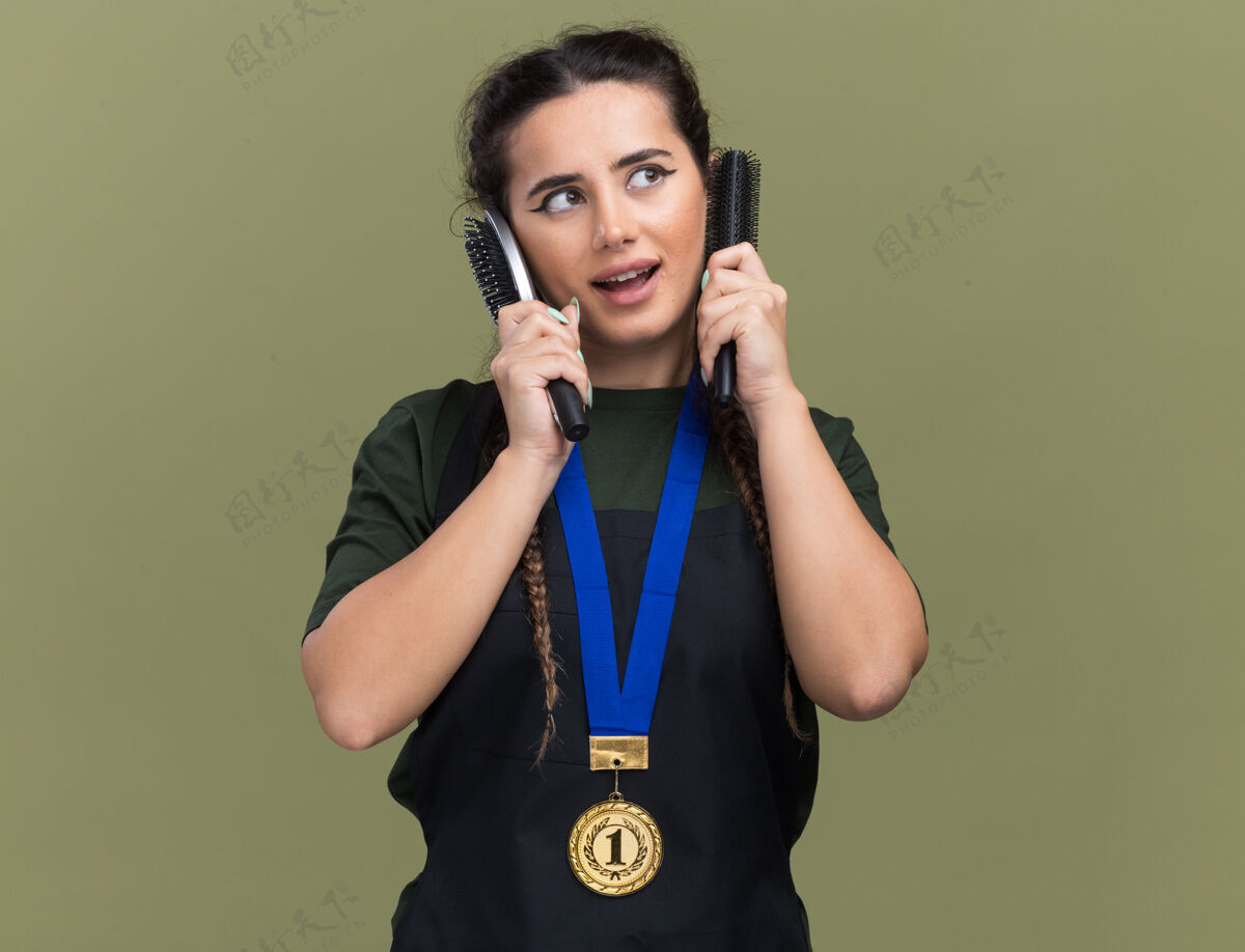 壁板一边高兴地看着年轻的女理发师穿着制服 拿着勋章的梳子绕着耳朵孤立地贴在橄榄绿的墙上人姿势感觉