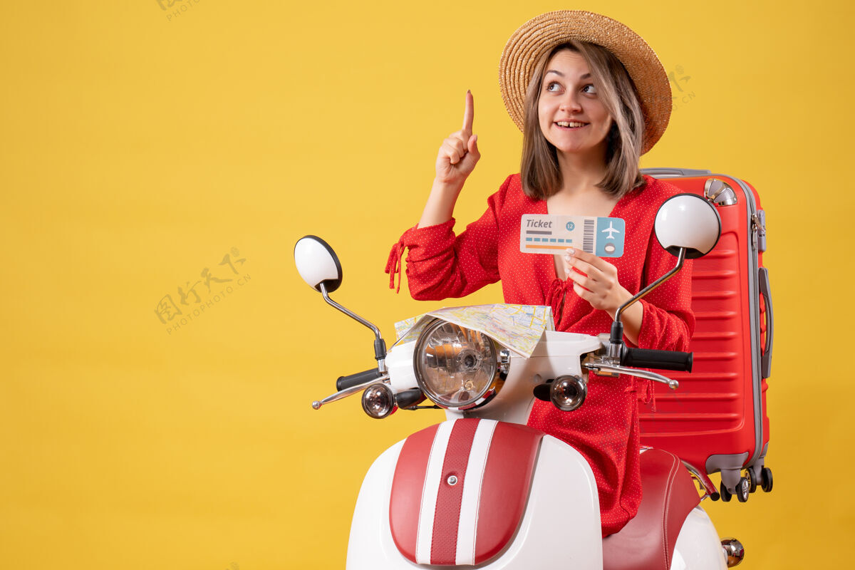 旅游正面图：穿着红裙子的年轻女士拿着票 手指着轻便摩托车女人手提箱冒险