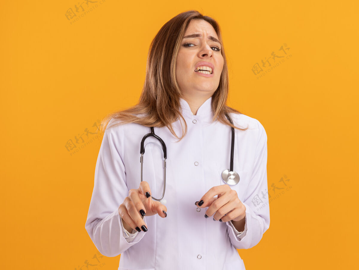 年轻人胆小的年轻女医生穿着医用长袍 黄色的墙上隔离着听诊器表情听诊器立场