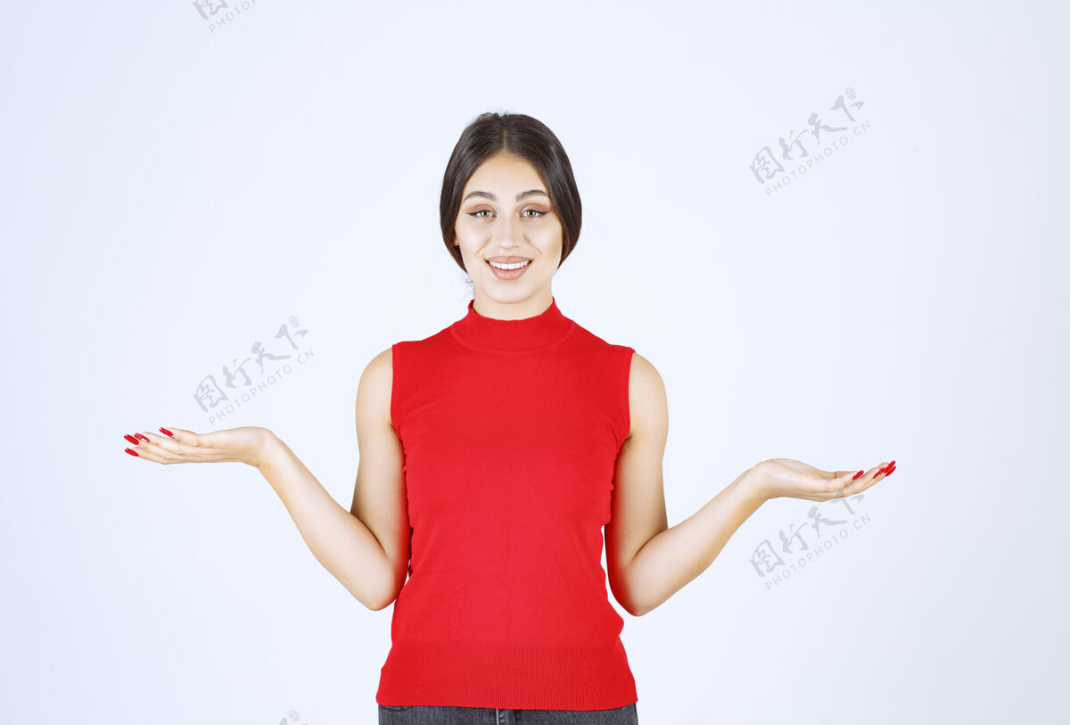年轻人穿红衬衫的女孩在她张开的手上展示着什么职员成人女人